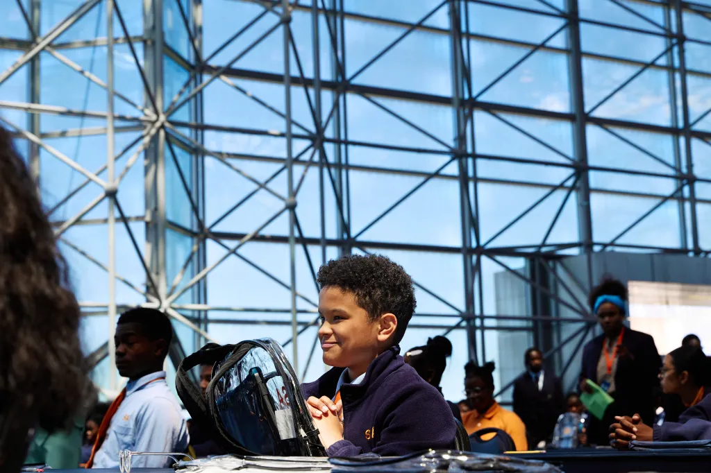 Young boy sitting at a desk with a clear backpack, smiling.