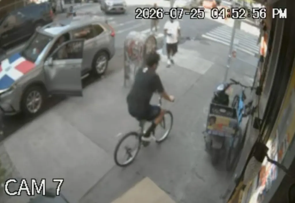 Surveillance footage of a person on a bicycle passing a car with a Dominican Republic flag on the hood and other pedestrians.
