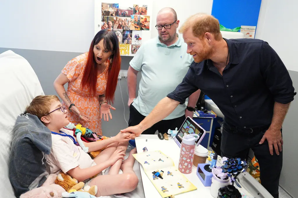 Prince Harry, in a blue shirt and black jeans, meeting Alec Hill, in a white T-shirt, who has a rare chromosomal condition and immune system disease, along with Alec's parents, at Birmingham Children's Hospital.