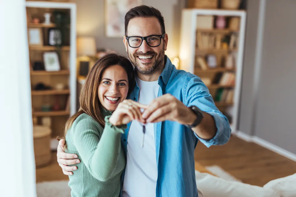 Happy couple embracing and smiling while holding new house keys.