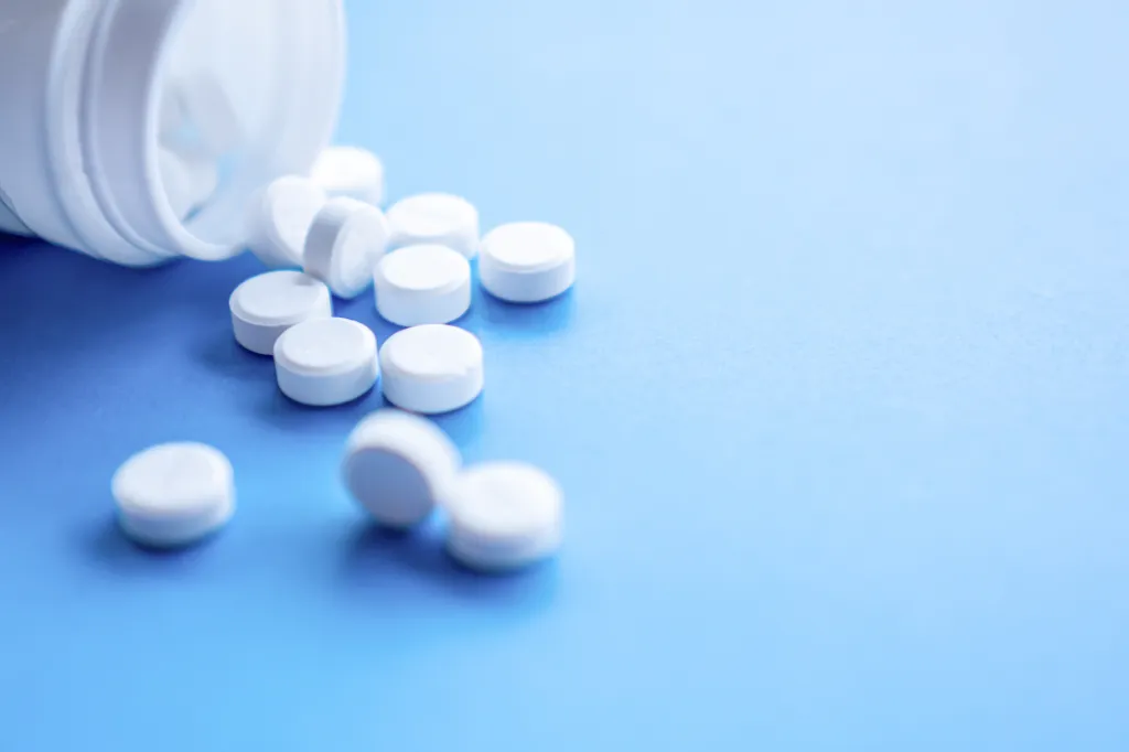 White pills spilling from a bottle onto a blue background.