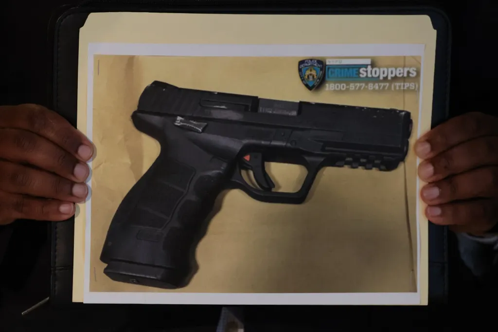 NYPD officer holding up a photograph of the firearm used in the shooting.