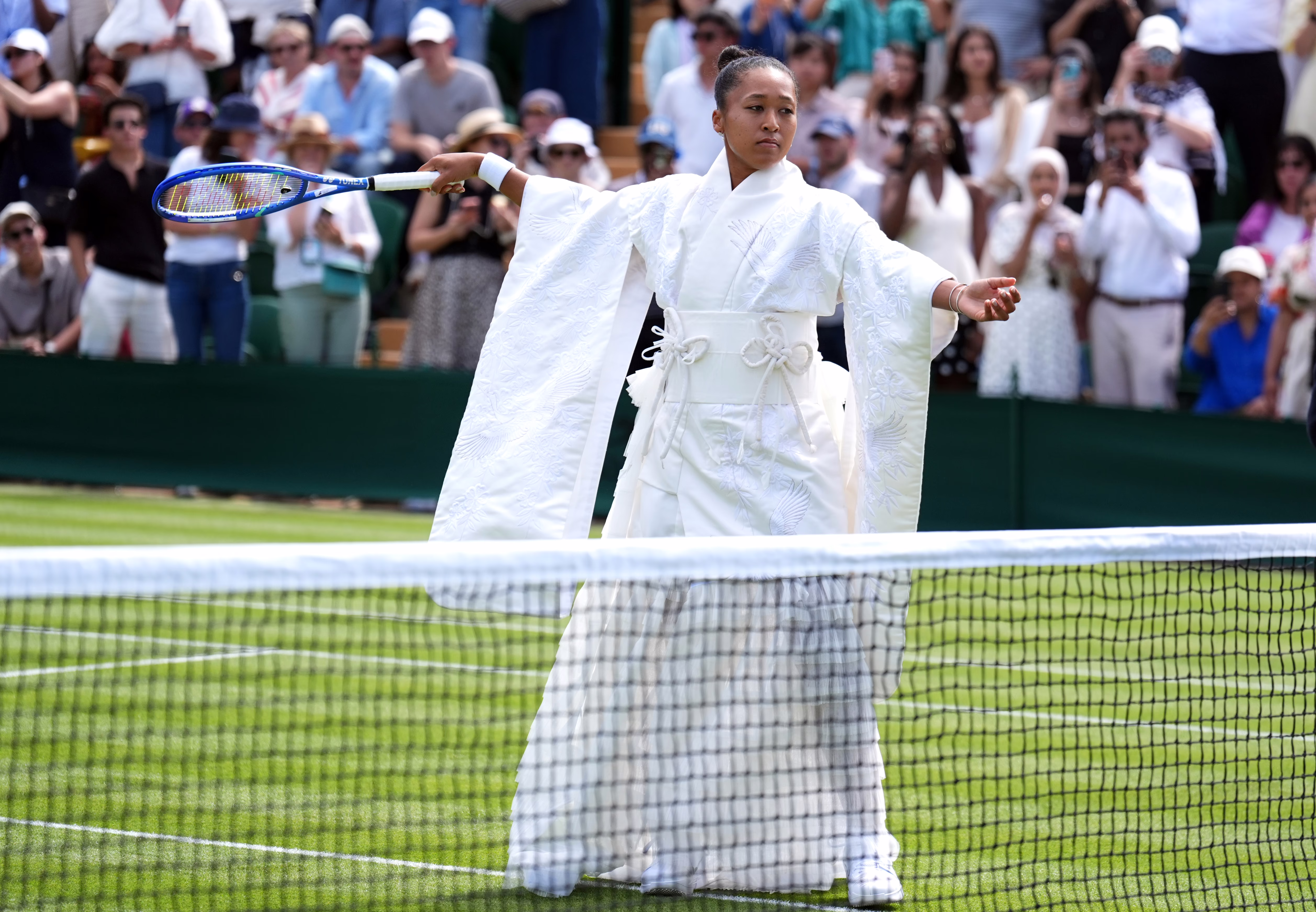 A tennis player stands on a court, wearing an all-white kimono outfit.