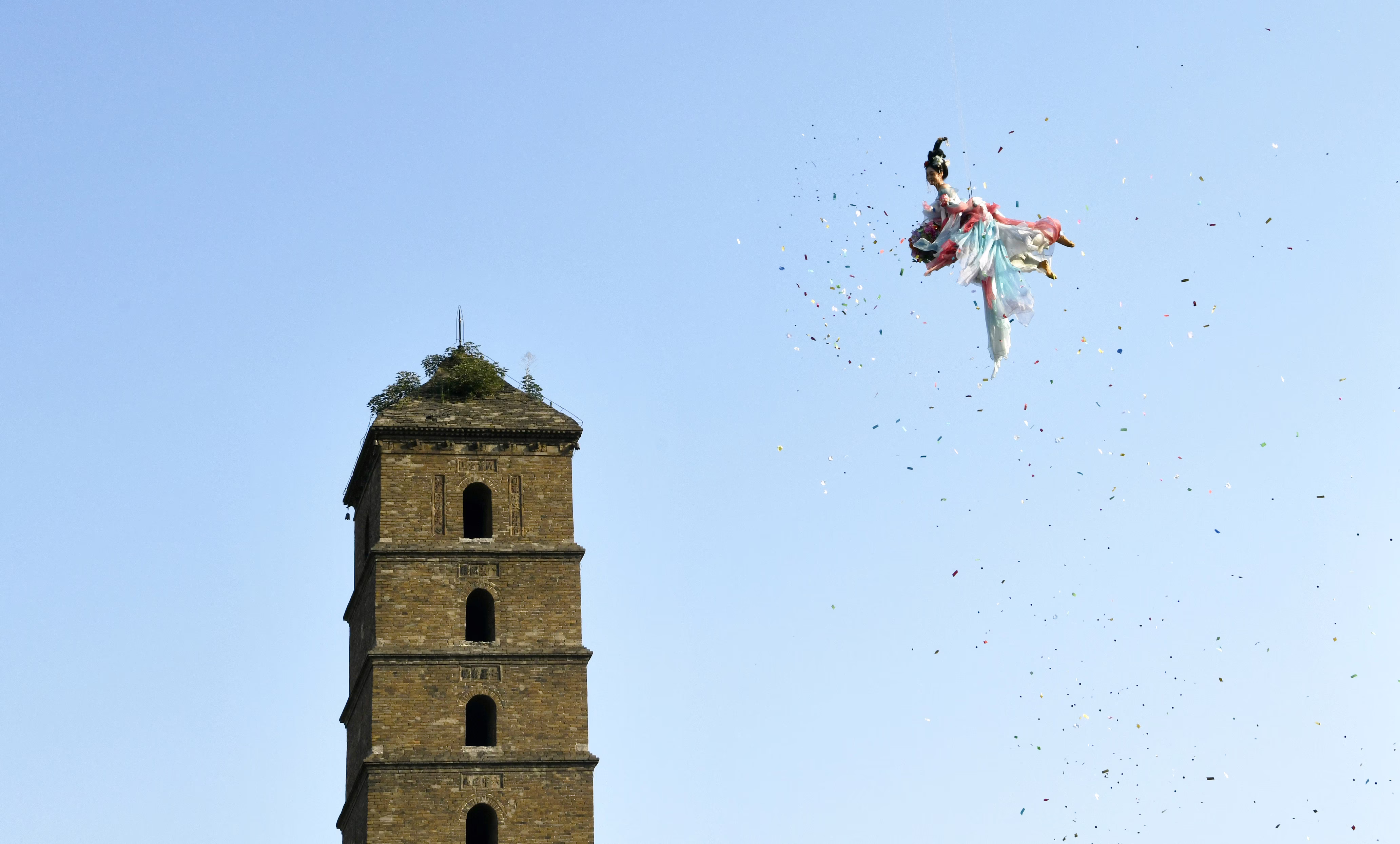 A person 'flies' through the air, suspended by cables, tossing peony petals.