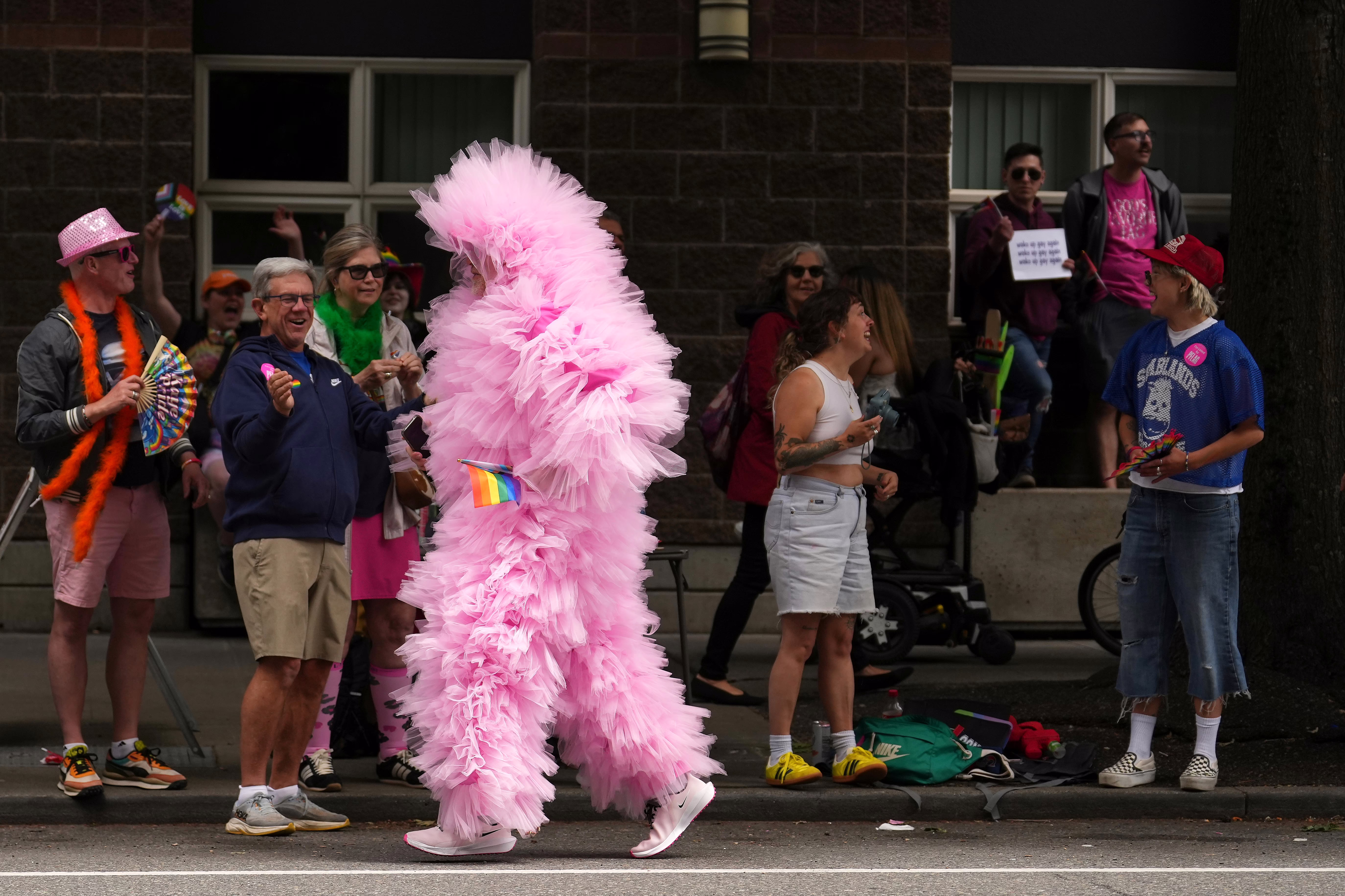 People at a Pride parade smile as a person jogs past, wearing a ruffly pink outfit from head to toe.