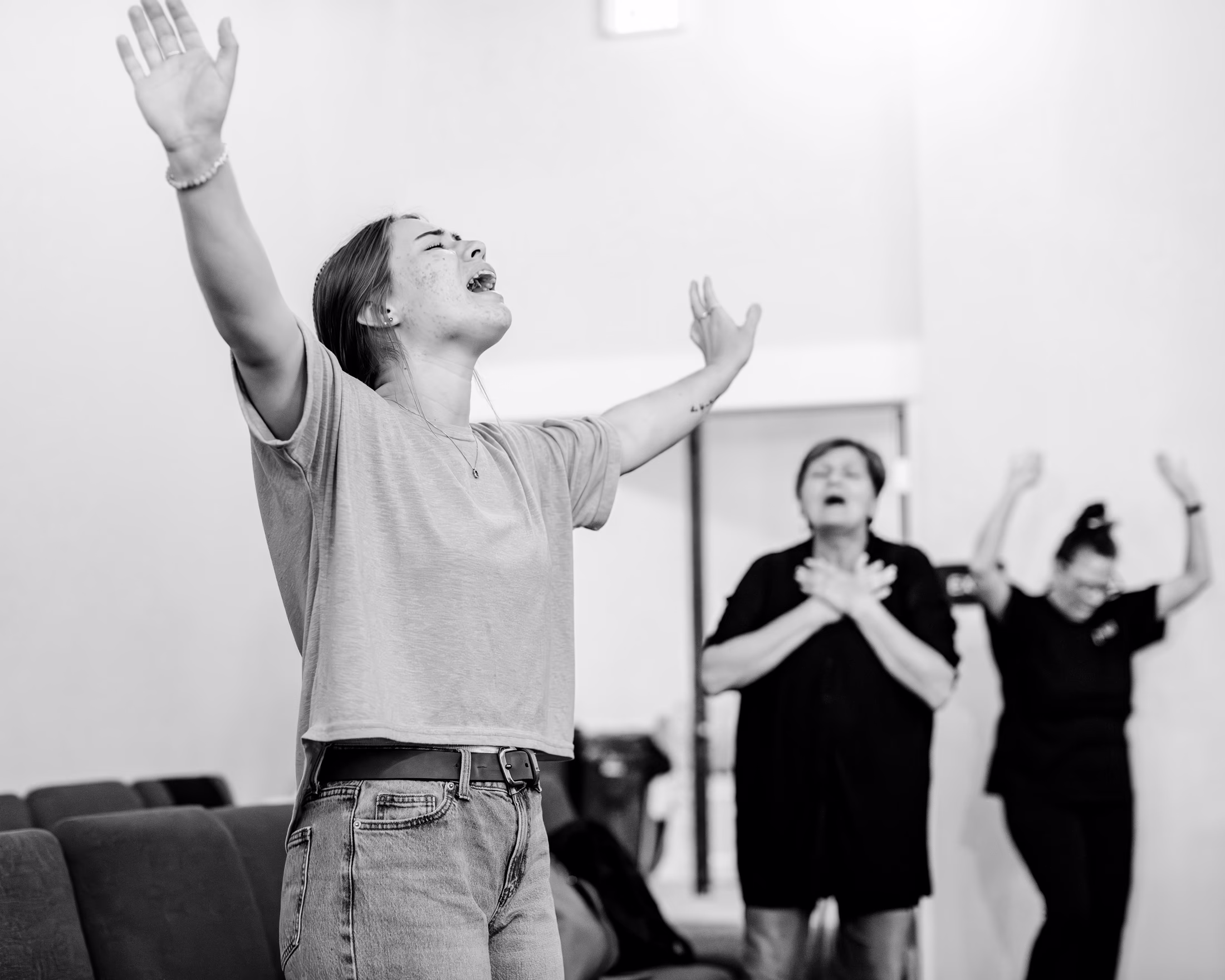 black-and-white photo of woman with arms up, eyes closed, and head back crying out, with other worshippers in background