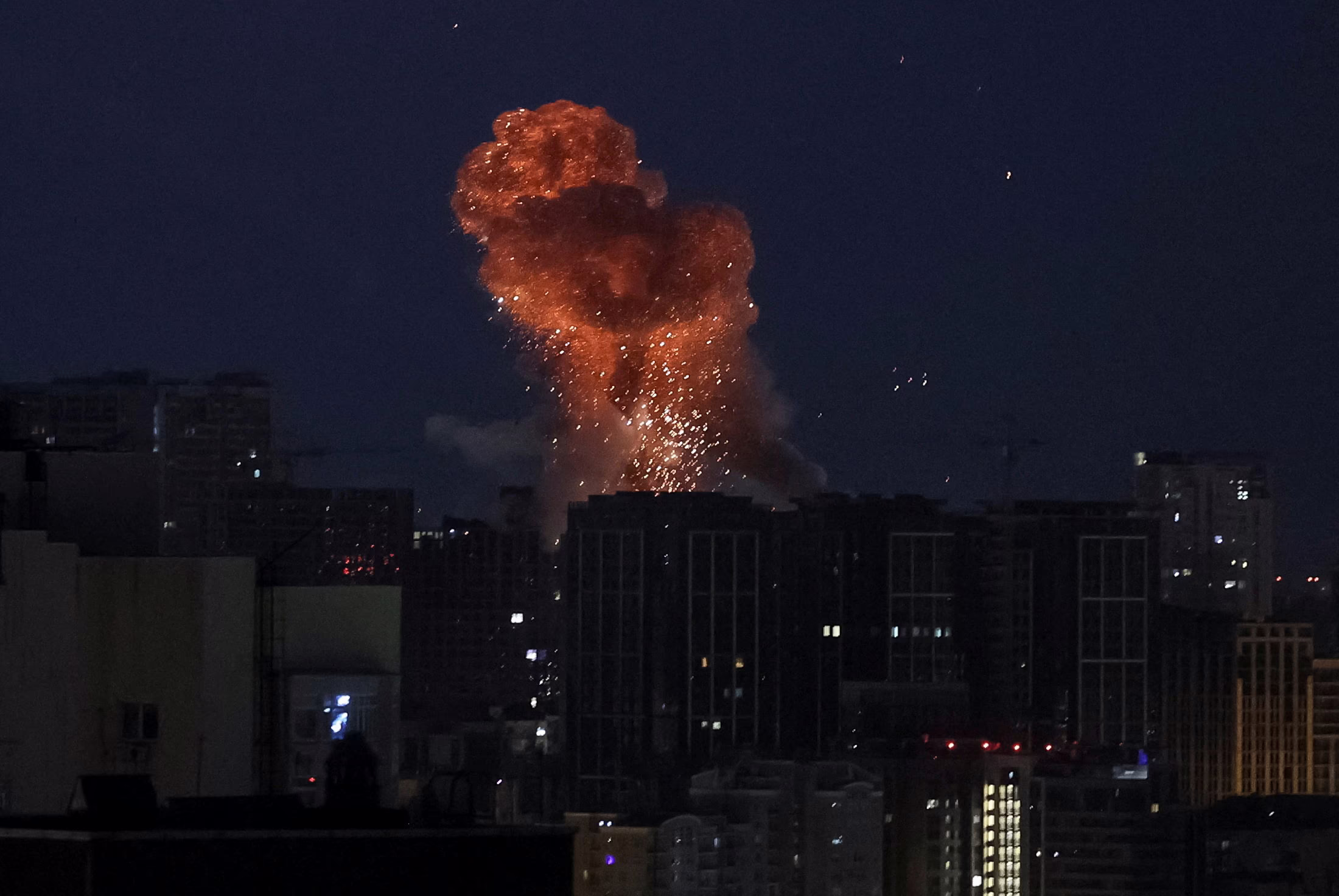 Smoke and sparks rise above a missile strike in a city, seen at night.