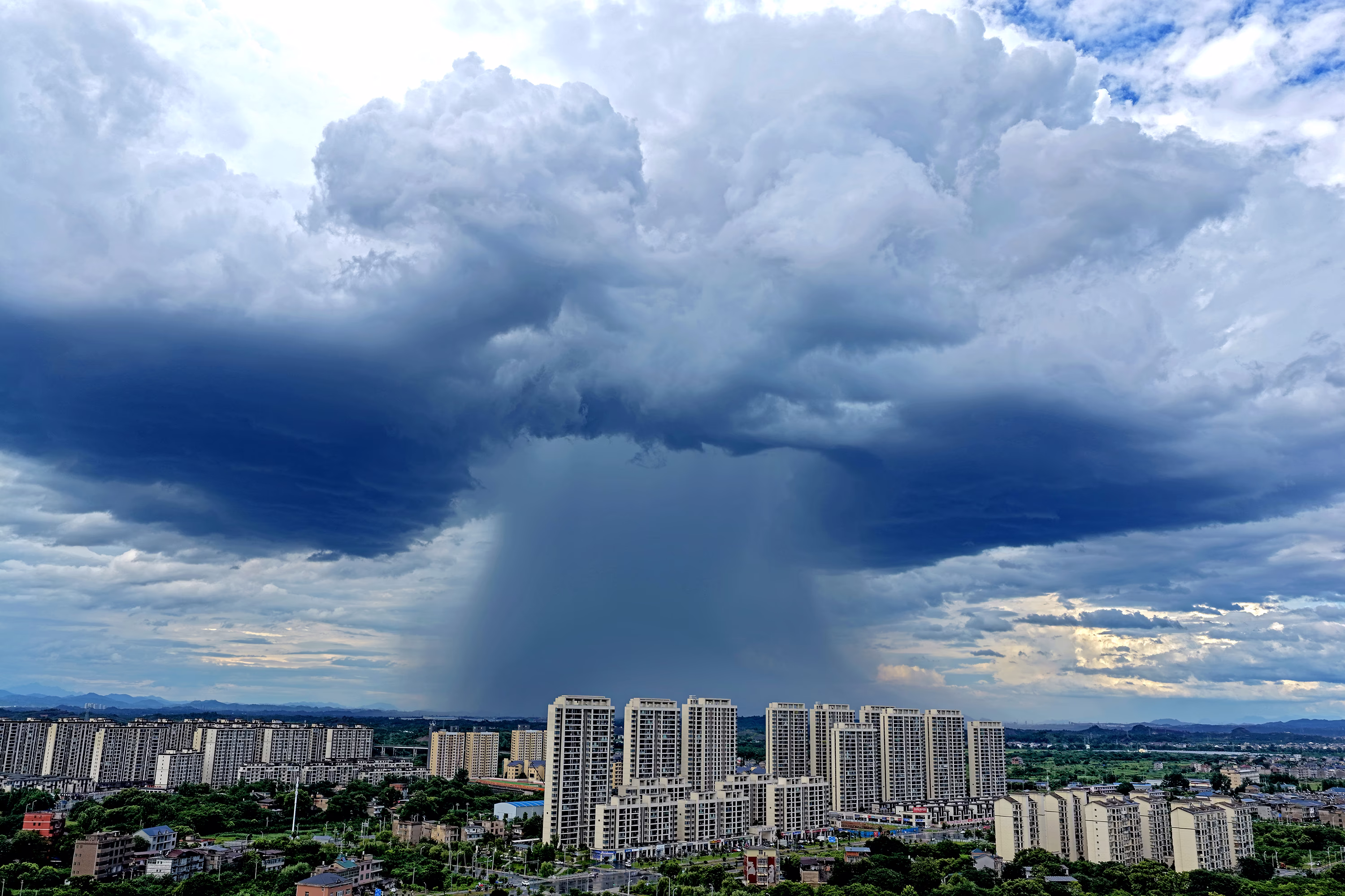 A huge column of heavy rain falls from a dark cloud above a city.