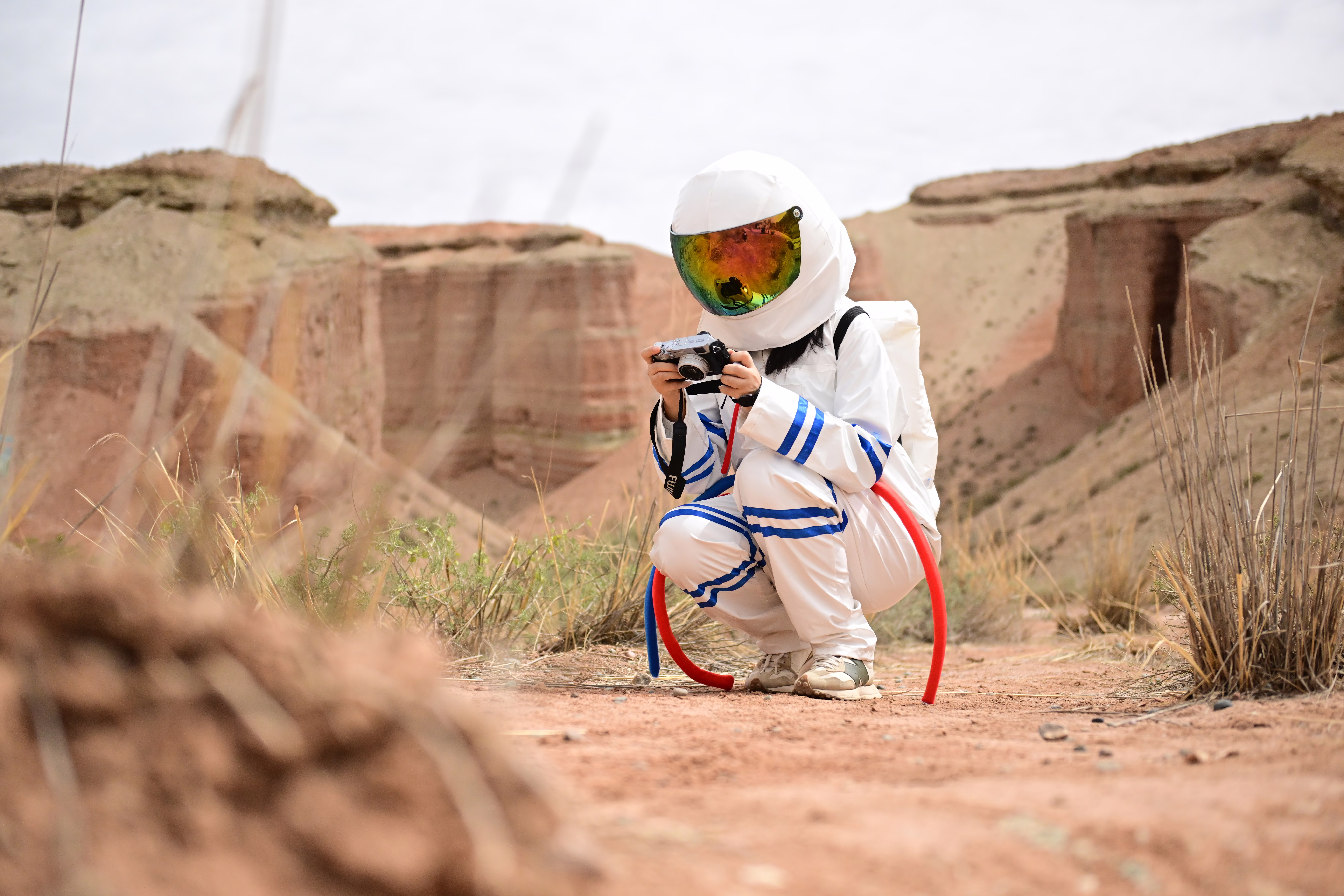 A tourist wearing an astronaut suit kneels down in a desert landscape.