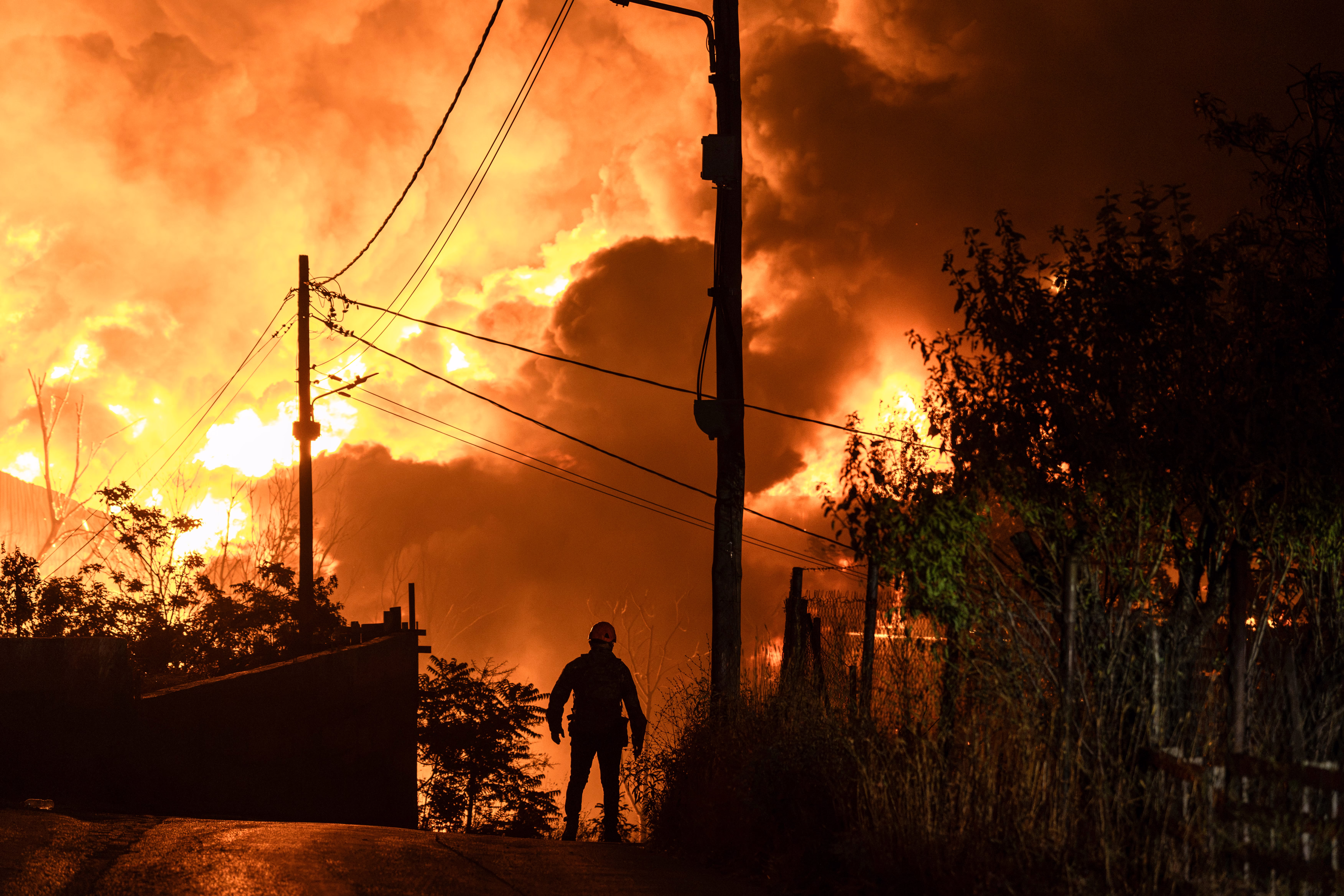 A rescuer, seen in silhouette, walks away from a burning factory.