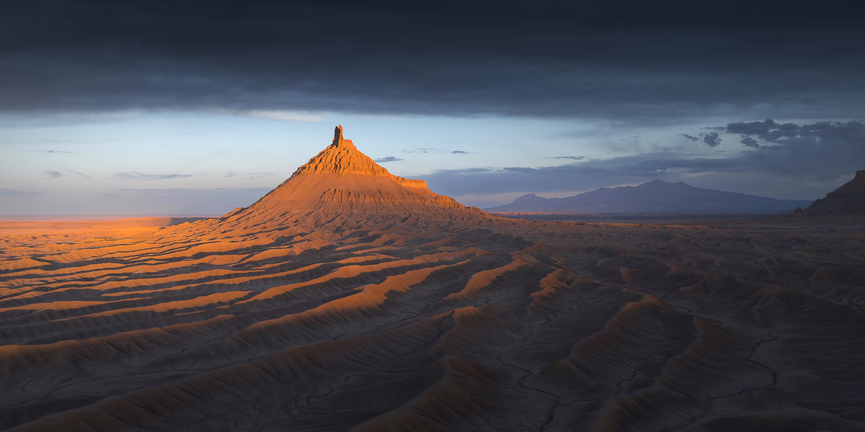 Sunset light over an iconic narrow butte, surrounded by a bare landscape of rippling ridges