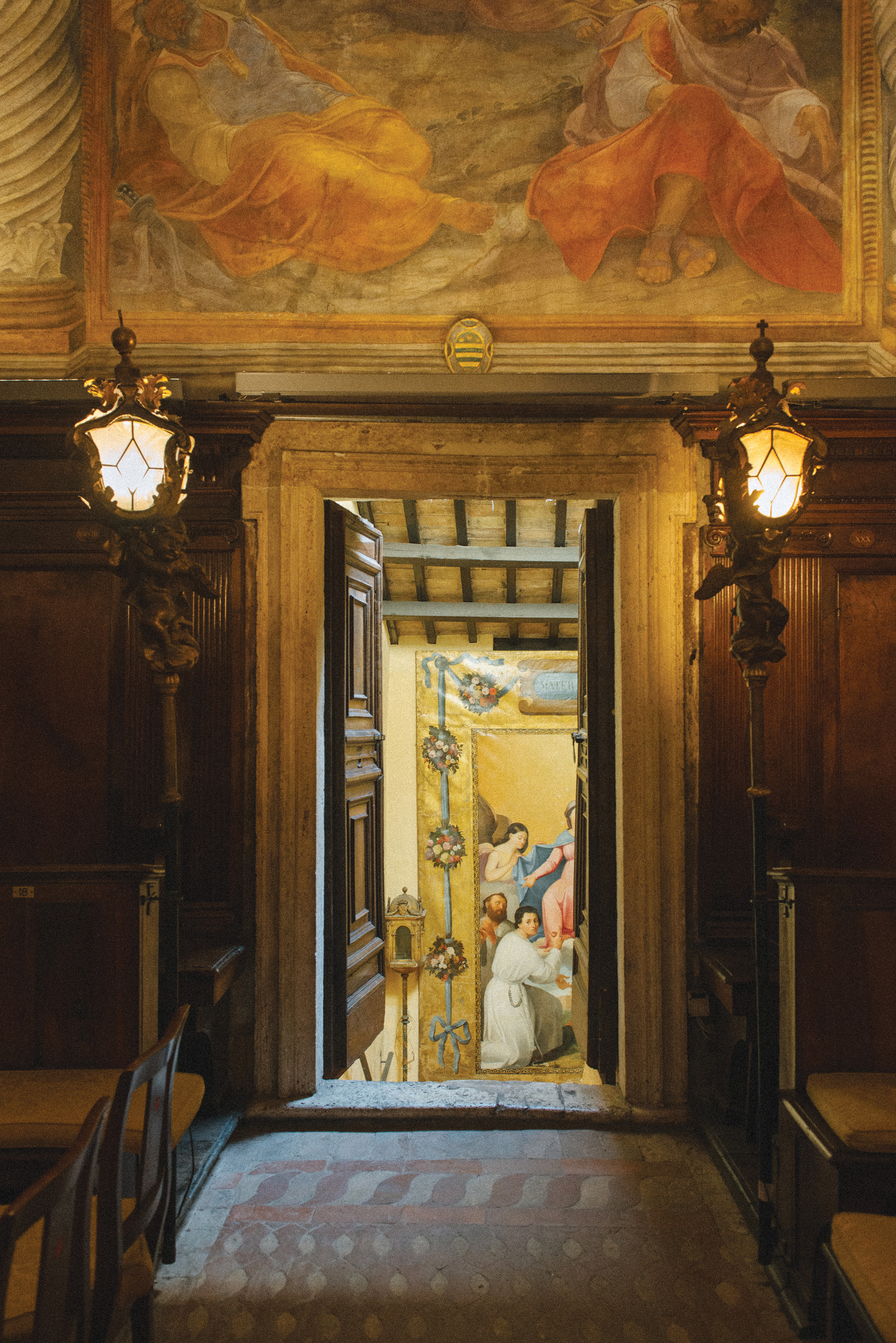 Color photo of Roman interior with ornate door flanked by large sconces opened to inner room.