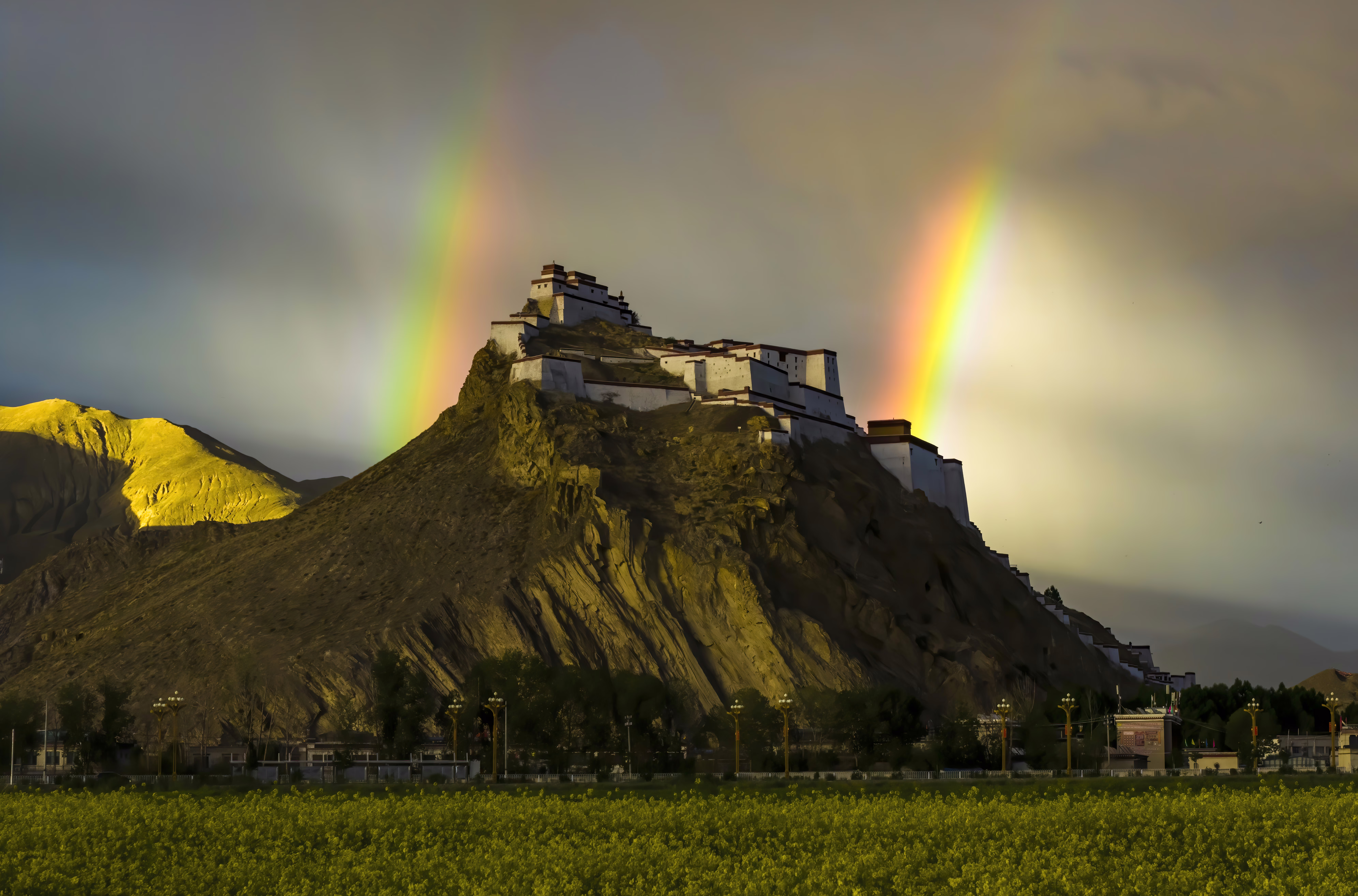 A double rainbow hangs in the sky above an ancient mountaintop fortress.
