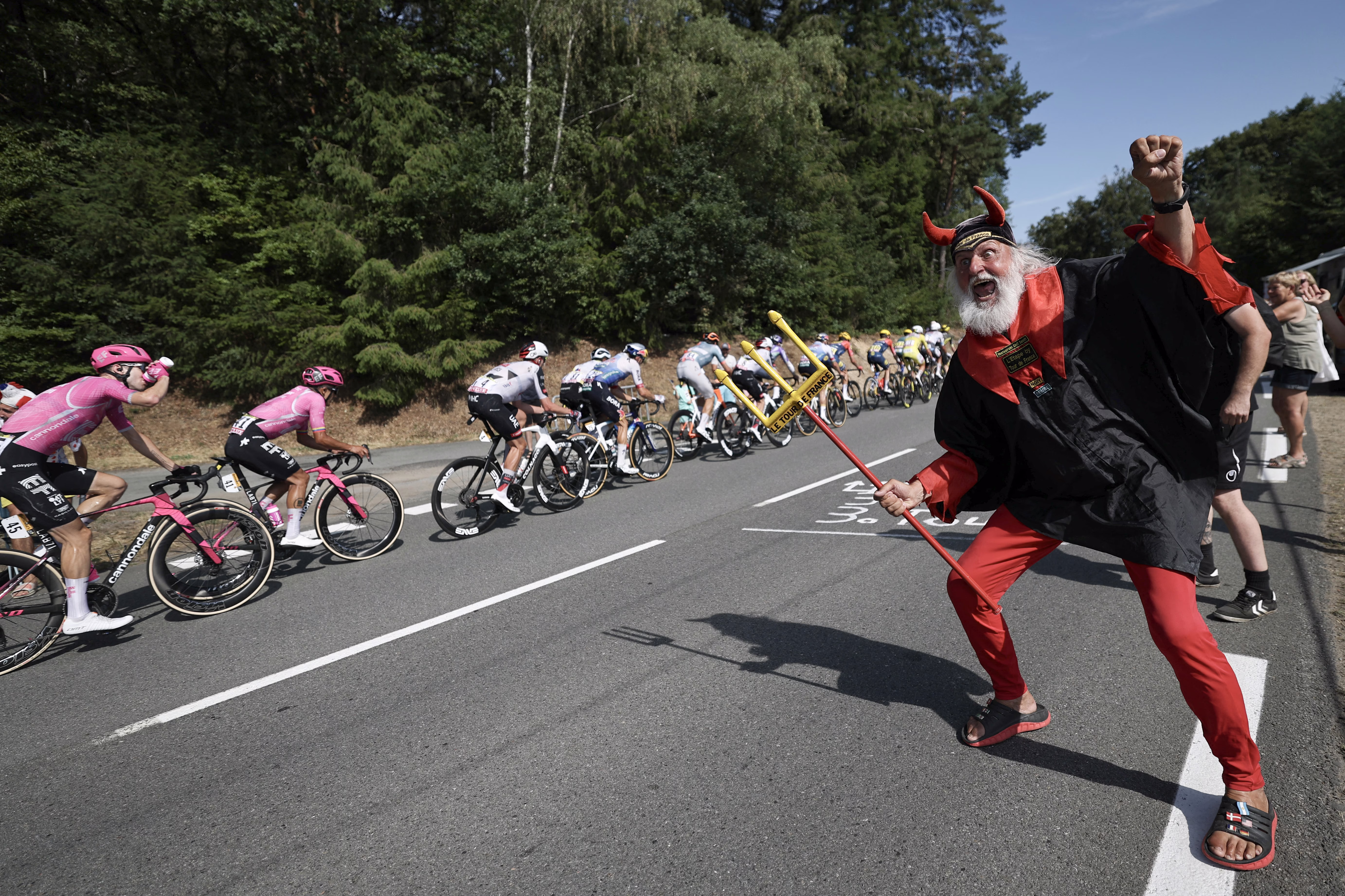 A fan dressed in a devil costume cheers as Tour de France cyclists pass by.