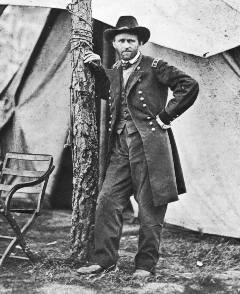 Ulysses S. Grant, in uniform, standing with his hand on a tree trunk.