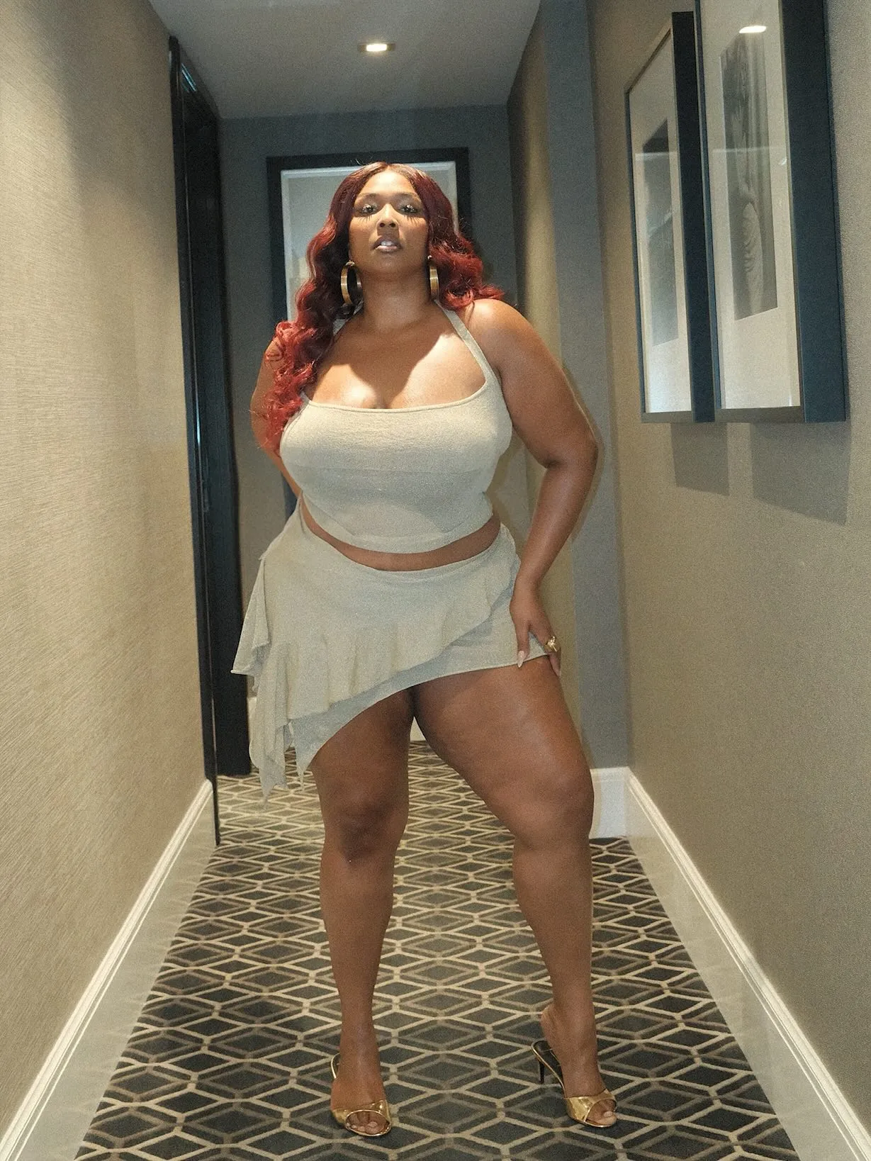 Lizzo posing in a hallway, wearing a light green halter top and matching asymmetrical ruffled skirt.