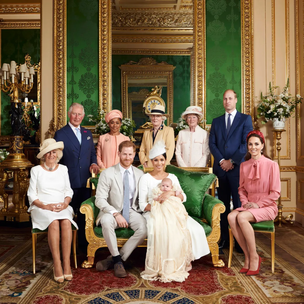 Official christening photo of Prince Archie. From left, Queen Camilla in a white dress and cream hat, King Charles in a blue suit and blue tie, Doria Ragland in a pink hat and pink coat, Lady Jane Fellowes in a tan jacket and cream hat with black trim, Lady Sarah McCorquodale, in a pink hat and pink coat, Prince William in a navy blue suit and blue tie, Kate Middleton In a pink dress and pink headband, Meghan Marke in a cream dress and cream hat, Archie in a cream christening gown, Prince harry in a light grey suit and blue tie. 