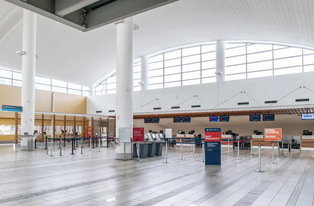 An empty airport check-in counter for Delta and JetBlue airlines, with stanchions and self-service kiosks.