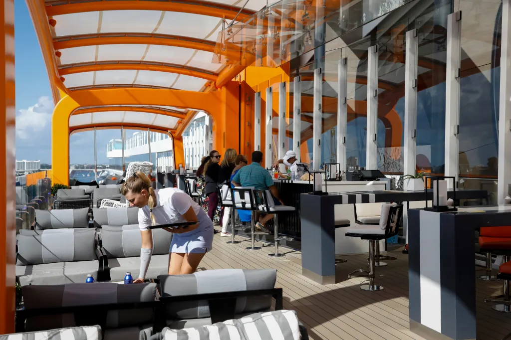 The Magic Carpet Restaurant on the Celebrity Beyond cruise ship, with customers at a bar and a server cleaning a table.