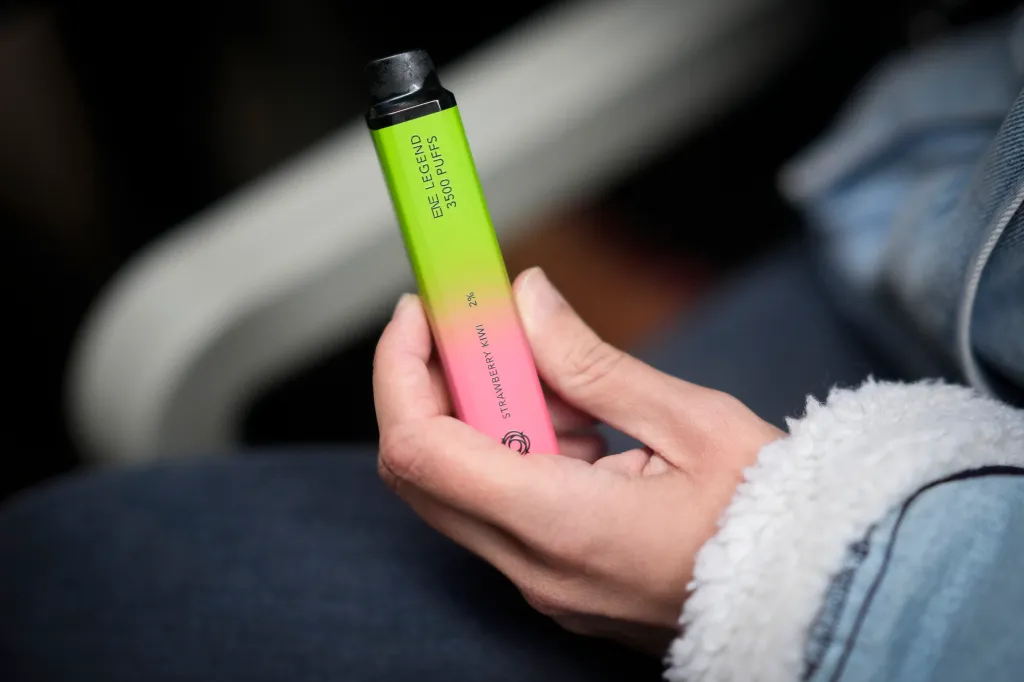 A woman holding a green and pink vape device labeled 