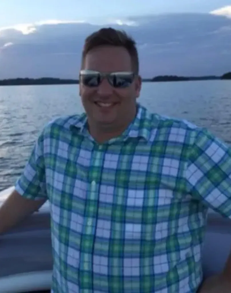 Matt Carney, owner of Smokin' Thighs, smiling while wearing sunglasses and a plaid shirt on a boat.