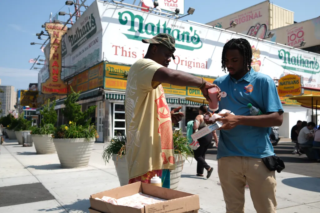 Two men sampling meatless hot dogs near Nathan's Famous.