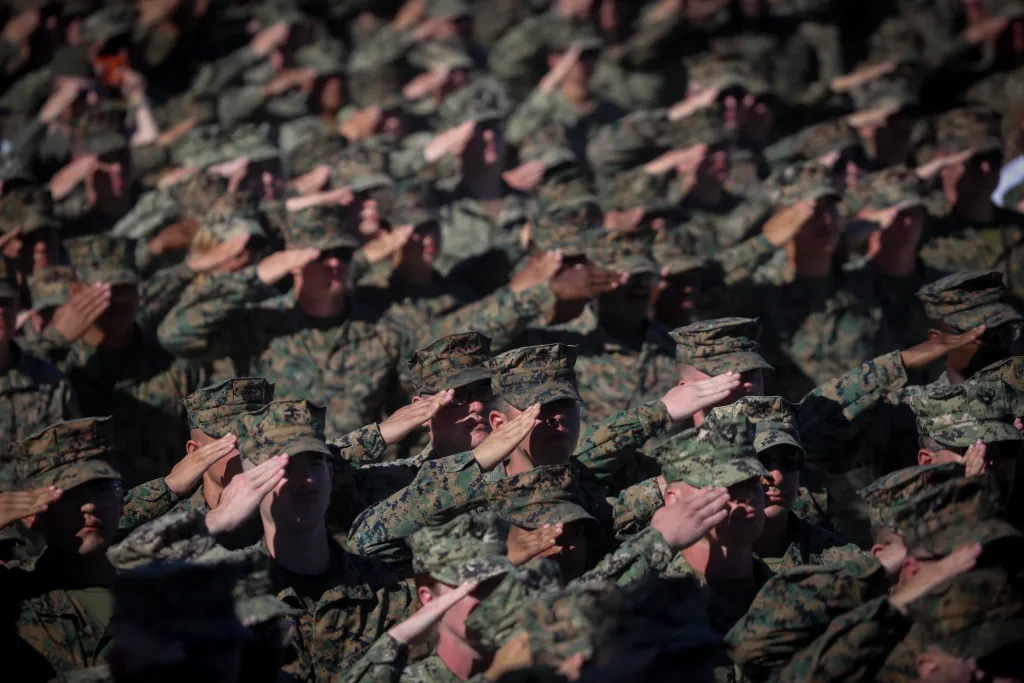 Members of the military in camouflage uniforms salute during the US Marine Corps 250th anniversary event.