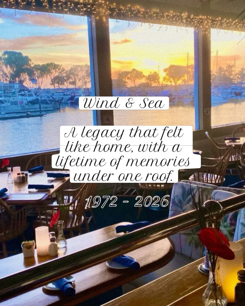 Interior of Wind & Sea restaurant with a view of Dana Point Harbor at sunset, with text announcing its closure.