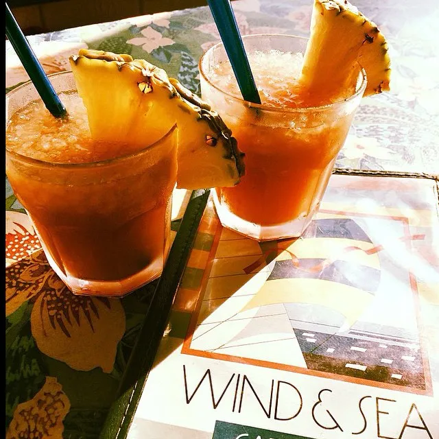 Two Mai Tai drinks with pineapple slices and straws on a table with a Wind & Sea menu.