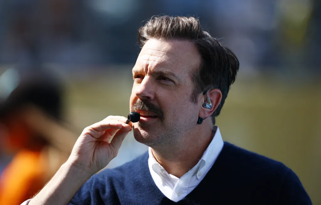 Actor Jason Sudeikis wearing an earpiece and holding a microphone to his mouth during the halftime show of the FIFA World Cup 2026 Final.