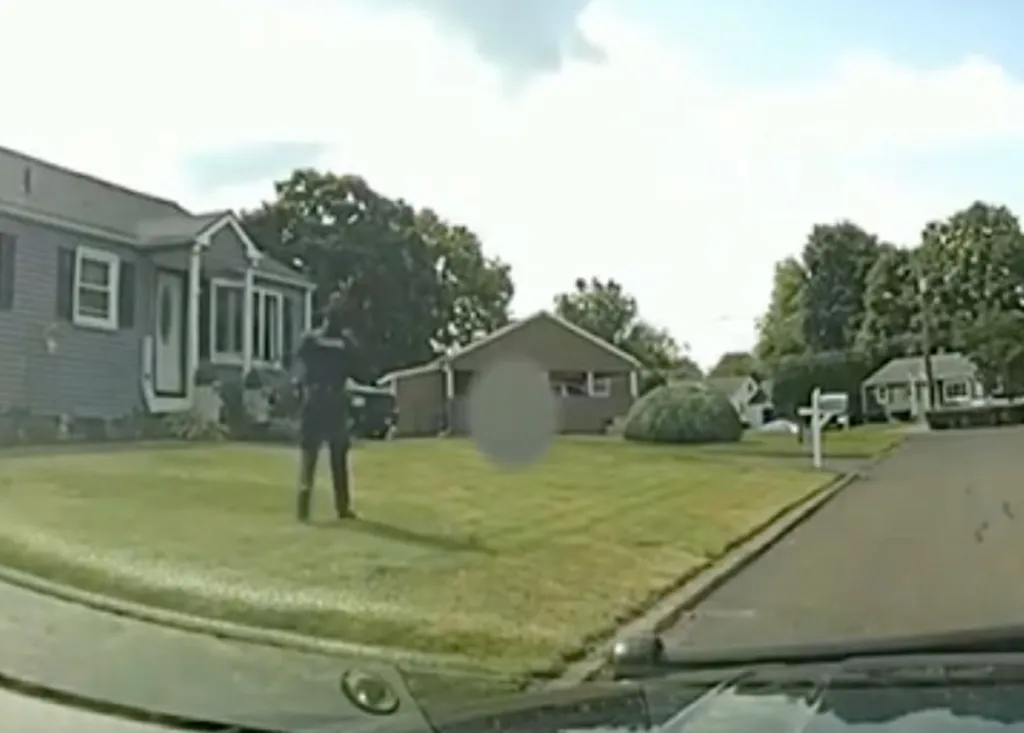 Footage from a car dashboard camera shows a police officer standing in a yard, with a blurred image of another person on the grass.