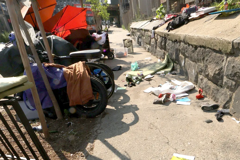 A homeless encampment with multiple large red umbrellas and belongings piled up along a city sidewalk.