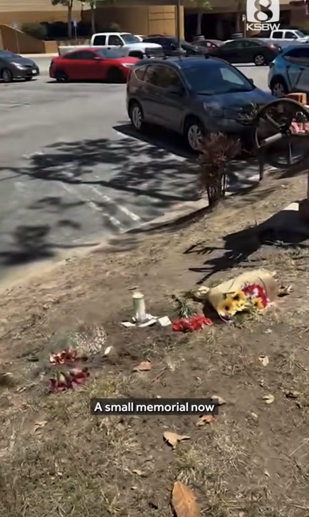 A roadside memorial in a parking lot with flowers and a candle.