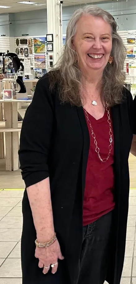 A smiling Rachell Summers, 73, wearing a black cardigan over a red shirt, and a long silver necklace.