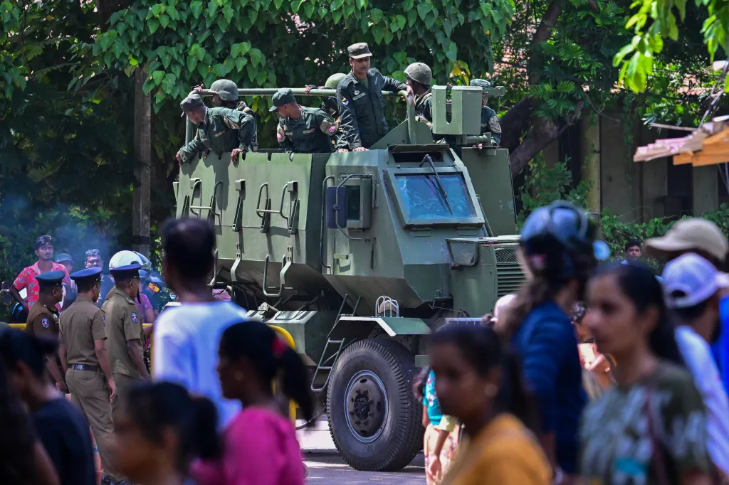 Army officers patrol near Negombo prison in an armored vehicle, surrounded by a crowd of onlookers and police officers.