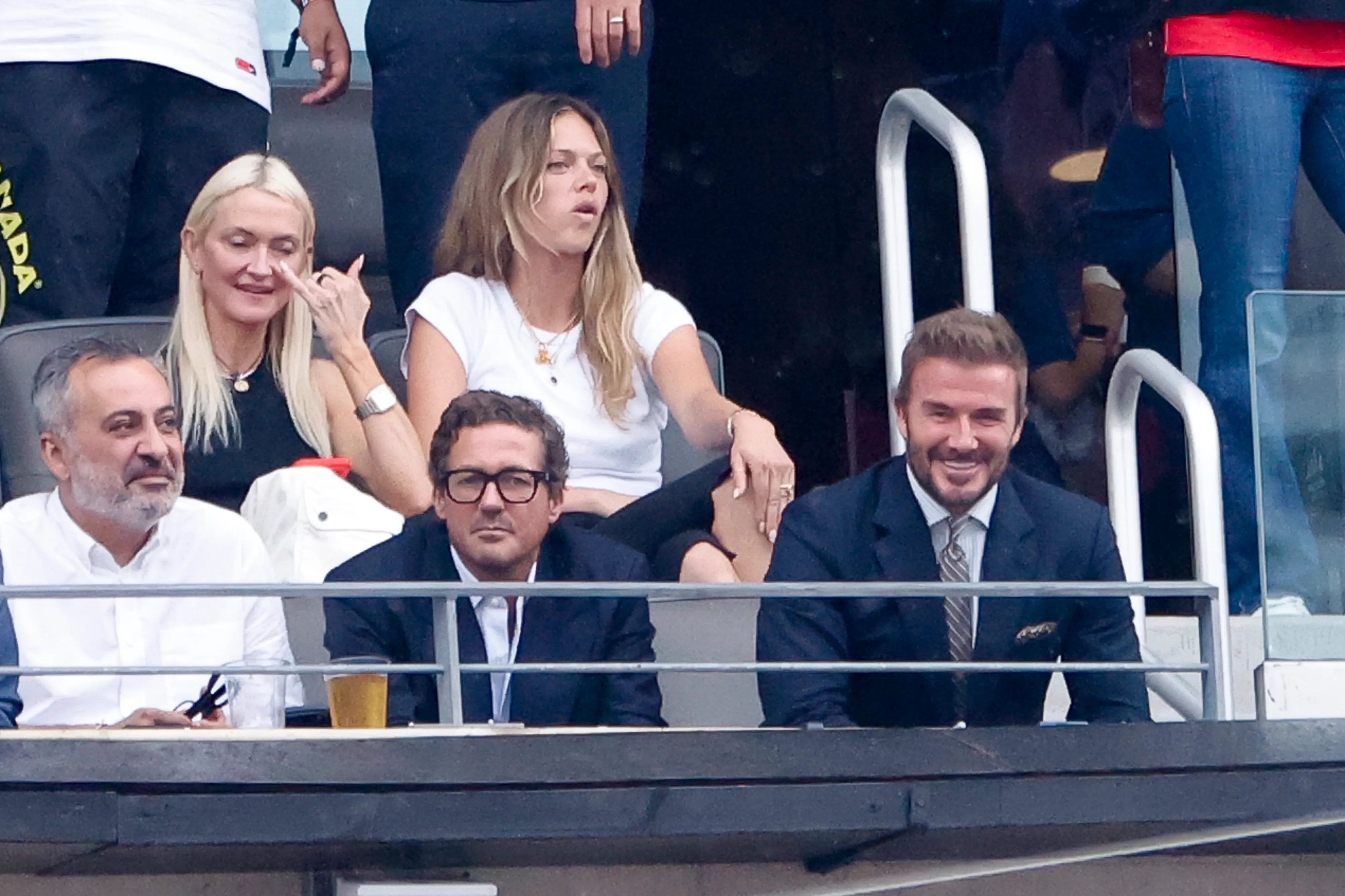 David Beckham and Dave Gardner in suits and other spectators watching a football match.