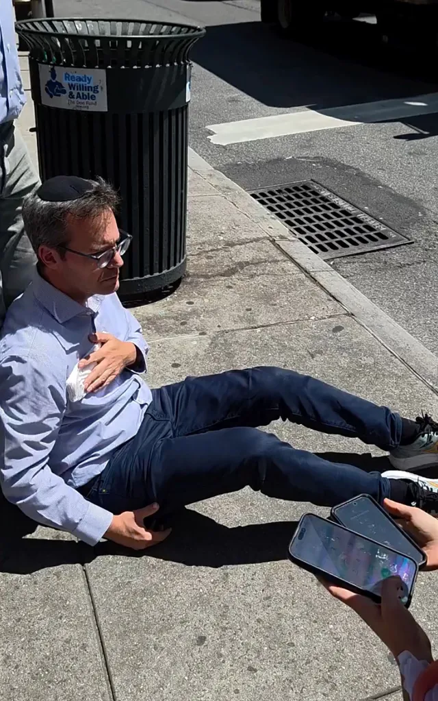 Moshe Grunhaus sitting on the sidewalk holding his chest after the stabbing.
