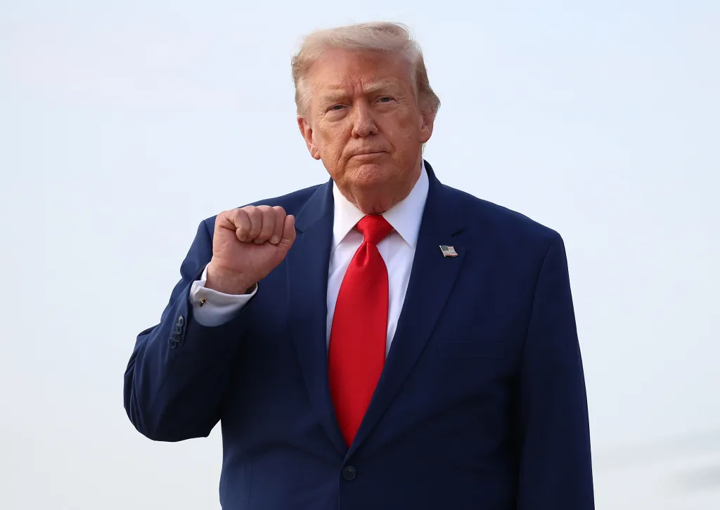 U.S. President Donald Trump, in a blue suit and red tie, makes a fist gesture while looking directly at the camera.