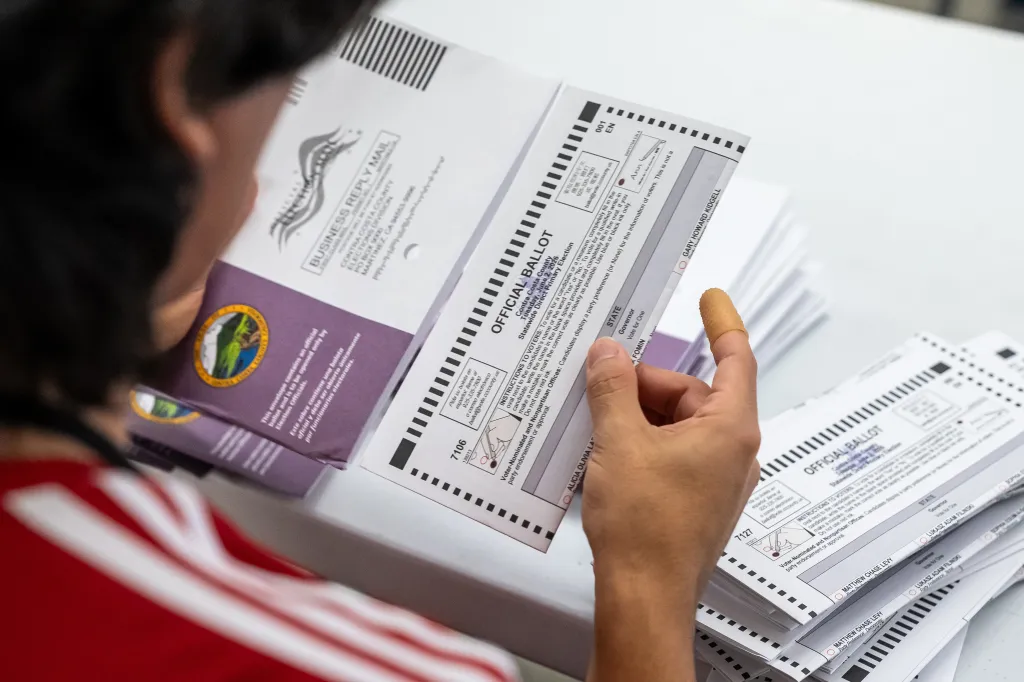 An election worker extracting a mail-in ballot from its envelope.