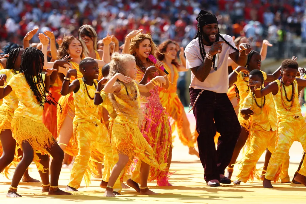 Shakira and Burna Boy perform on stage with dancers in yellow and orange outfits at the FIFA World Cup 2026 halftime show.