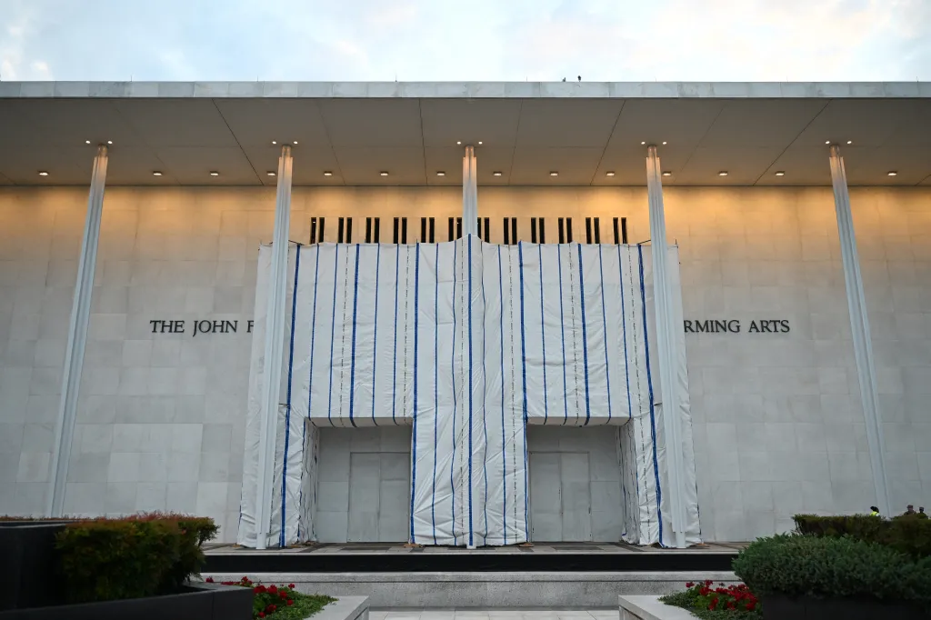 Facade of The John F. Kennedy Center for the Performing Arts with its entrance covered by white tarp with blue stripes.