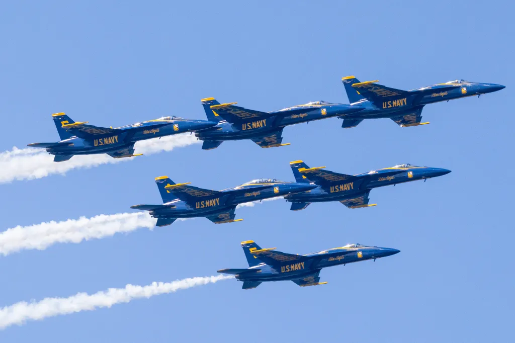 Six U.S. Navy Blue Angels jets flying in formation against a clear blue sky, leaving white contrails.