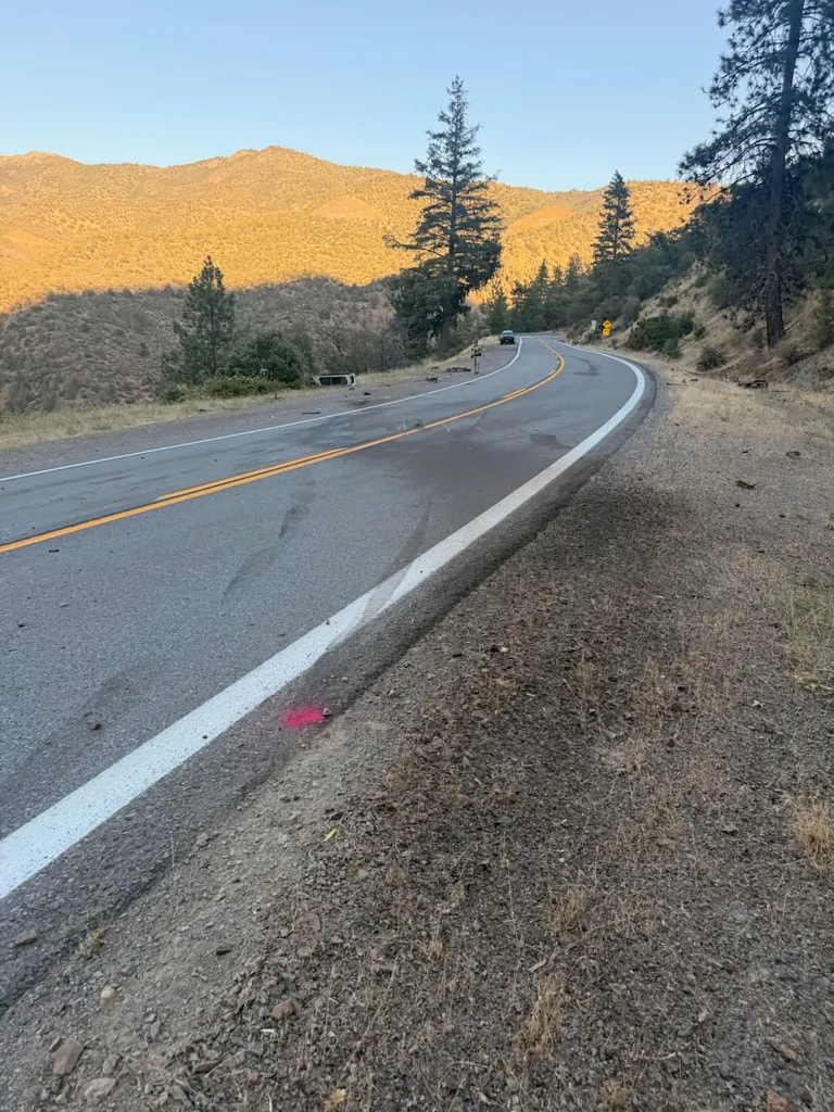 A winding rural highway with debris, tire marks, and survey markers visible near the side of the road, indicating a vehicle left the roadway.