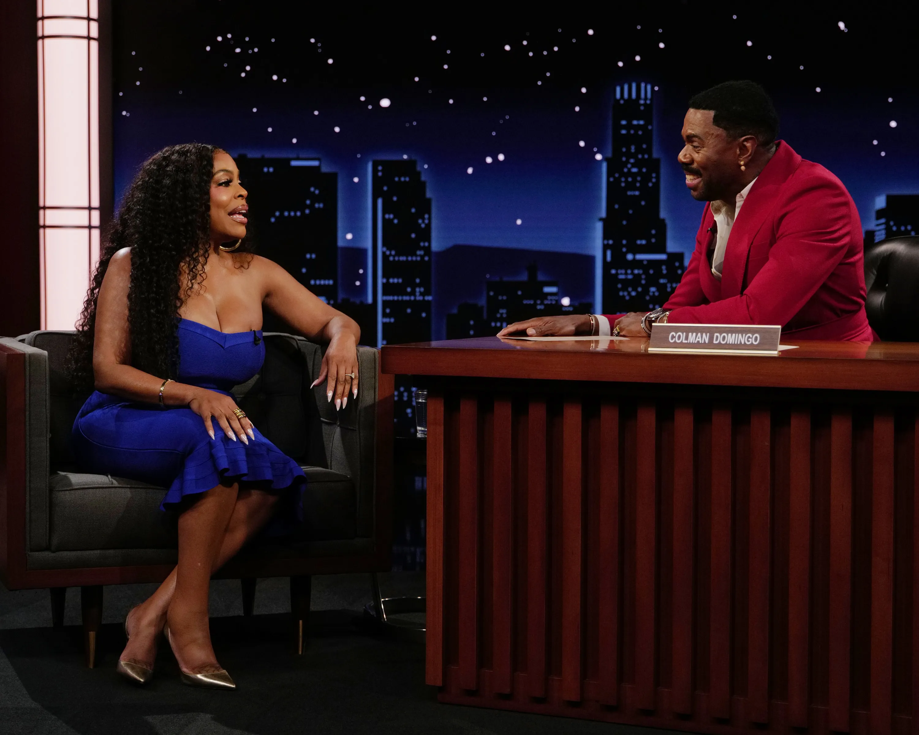 Niecy Nash-Betts in a blue dress and Colman Domingo in a red suit on a TV set.