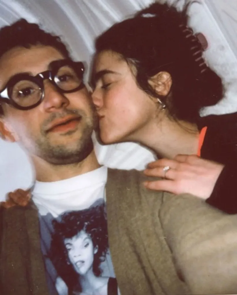 A woman kissing a man with black, thick-rimmed glasses on the cheek.