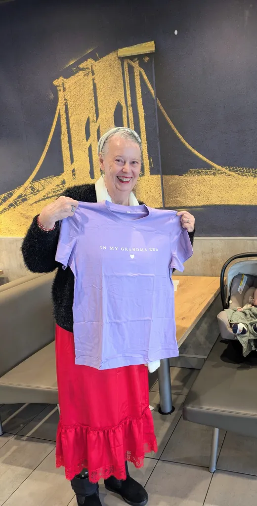 A woman smiling while holding a lavender t-shirt that reads 