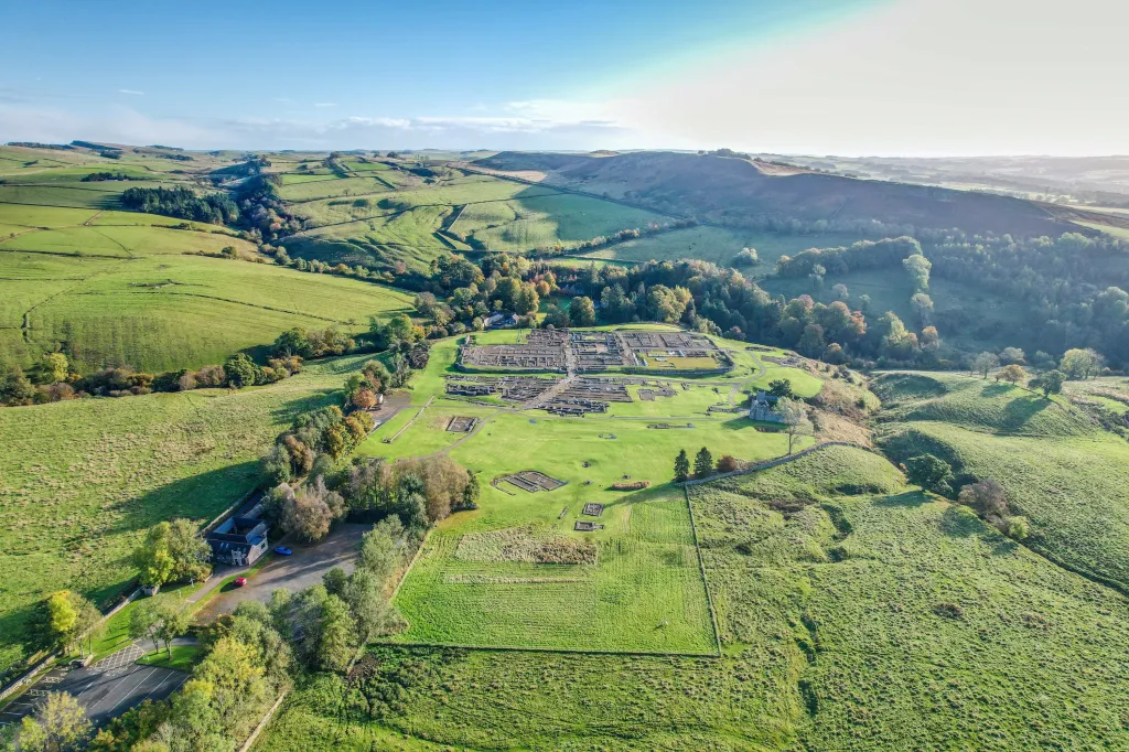 Aerial view of Vindolanda Roman fort surrounded by green fields and rolling hills.