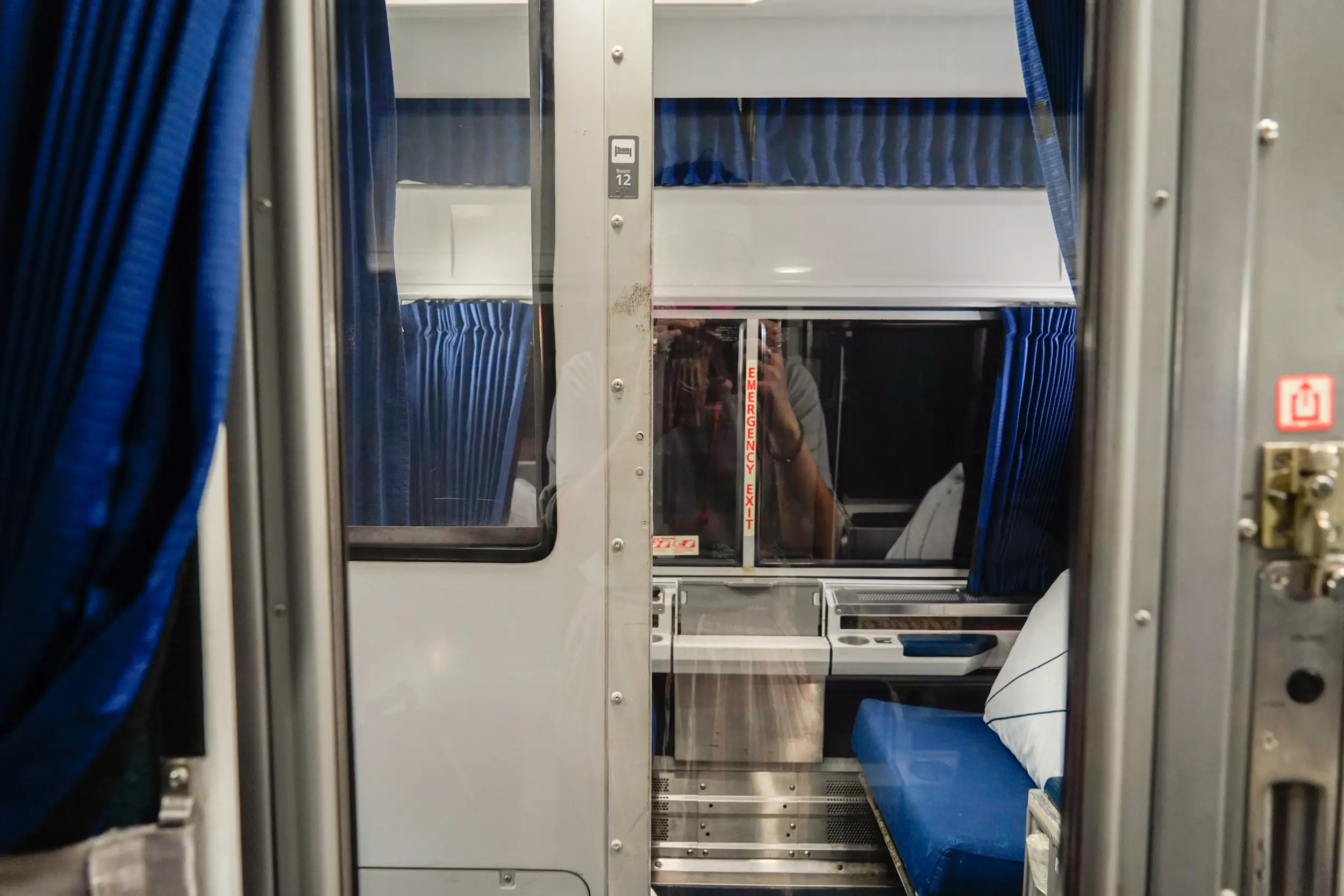 A view of an empty roomette with blue seating and curtains on an Amtrak overnight train
