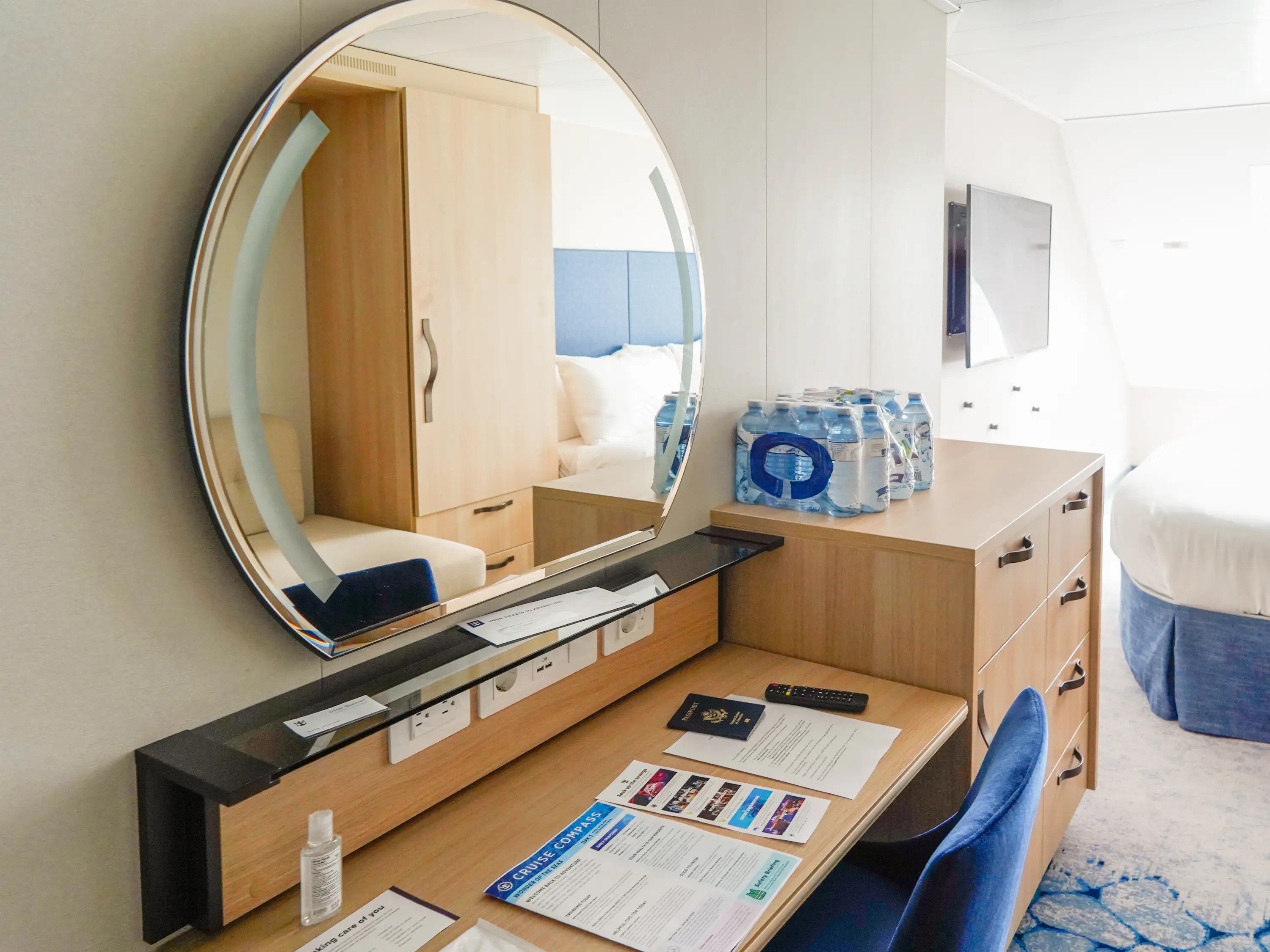A desk in a cruise cabin with a circular mirror above it