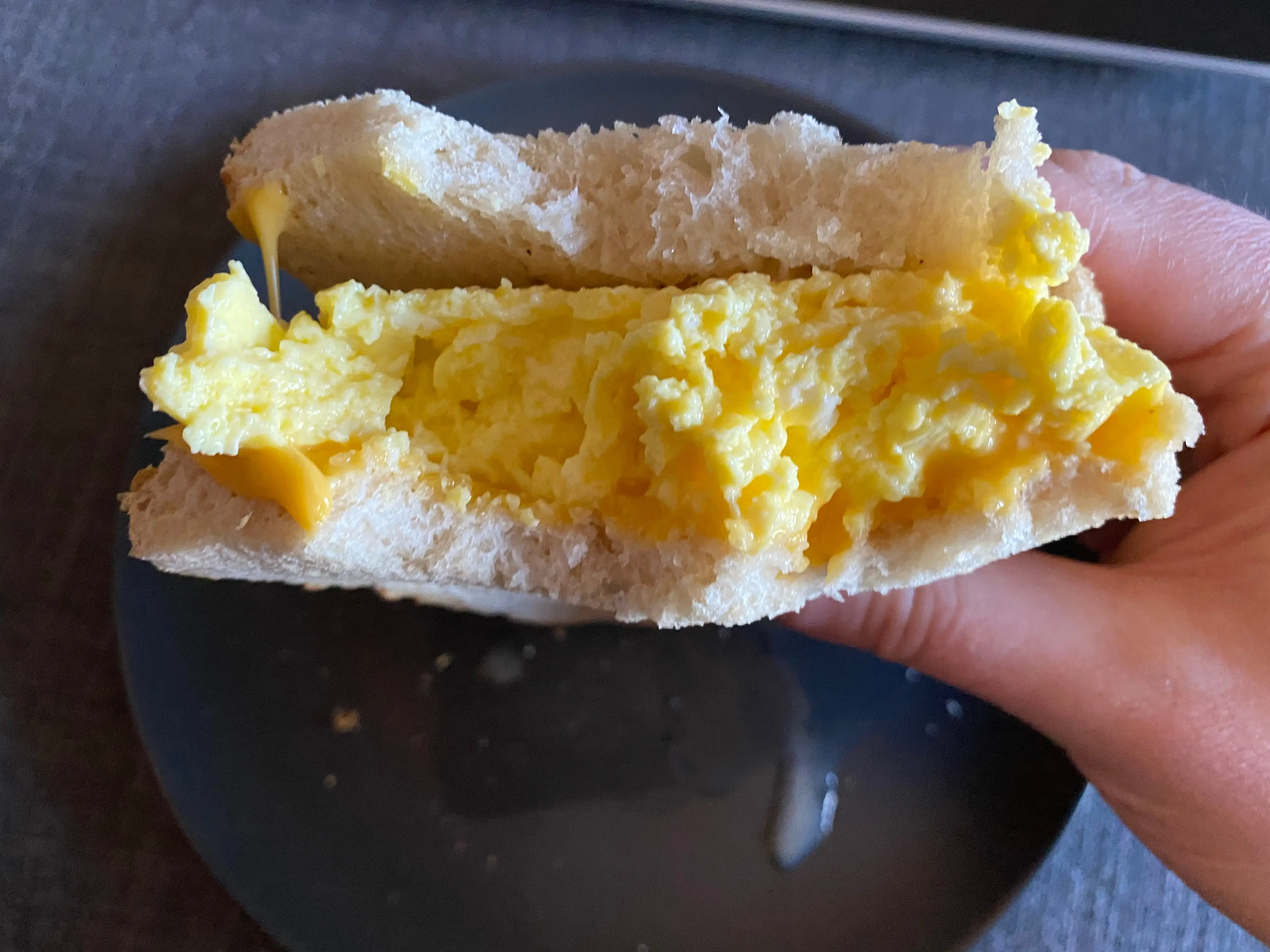 The writer holds a sandwich with scrambled eggs and a few bites taken out of it over a blue plate